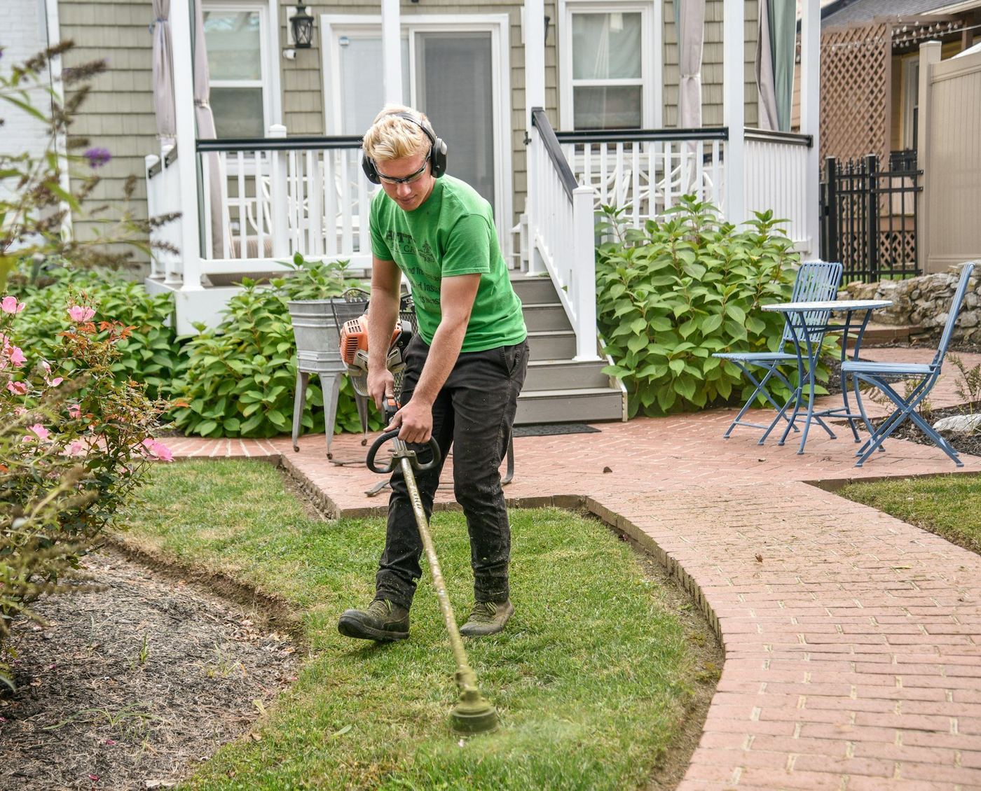 Jardinier utilisant une débroussailleuse thermique le long d'une allée de jardin